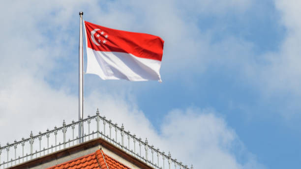 Singapore flag waving atop a building with red-tiled roof against a blue sky with clouds, conveying a sense of national pride.
