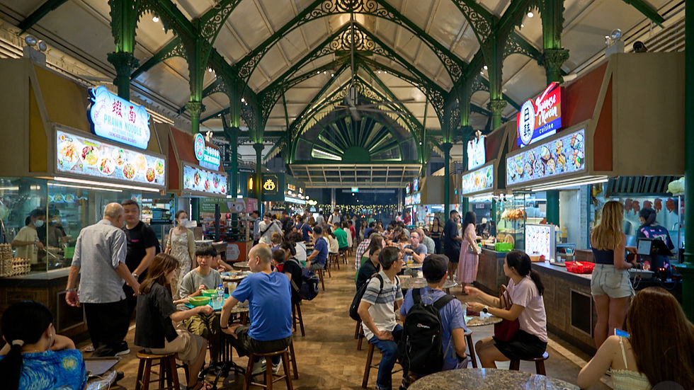 People dining and talking at a lively food market with green arches and bright food stall signs. An atmosphere of bustling enjoyment.