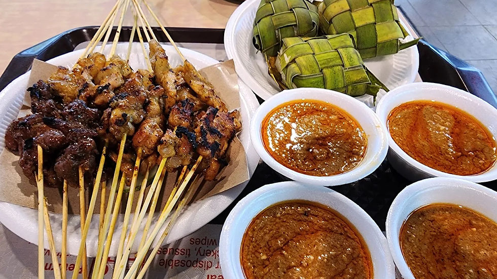 Skewered grilled meat with sizzling char, three bowls of spicy peanut sauce, and woven green rice parcels on plates, create a feast.