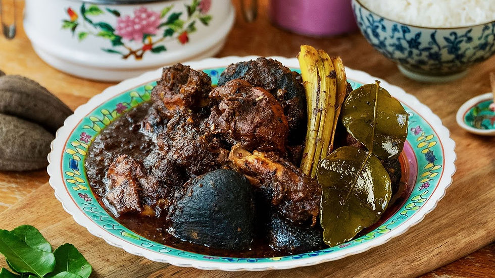 Braised beef dish with spices and leaves on a floral plate, set on a wooden table with bowls of rice. Rich, hearty, and aromatic.