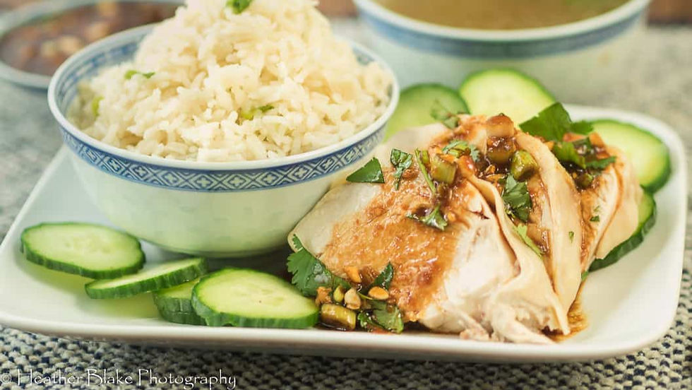 Plate with sliced chicken, topped with herbs and sauce, beside cucumber slices. Bowl of rice in blue-patterned dish. Casual setting.