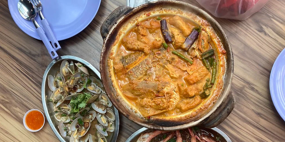 Overhead view of a wooden table with a bubbling orange seafood curry, clams in a metal dish, and purple plates.
