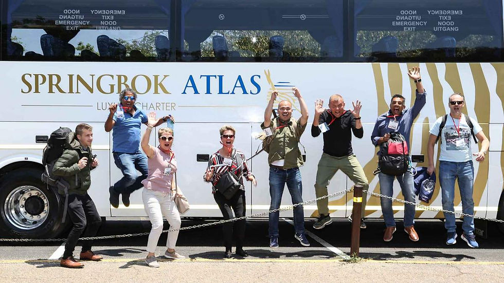 Group of people joyfully jumping in front of a white "Springbok Atlas" bus with patterned stripes. Bright and cheerful mood.