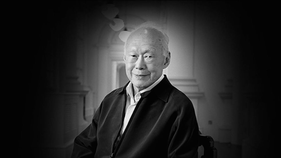 Elderly man in a dark jacket sits against a blurred indoor background. Black and white image conveys a serene and introspective mood.