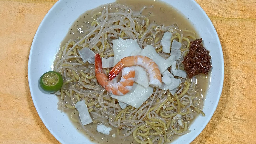 White plate with noodles topped with shrimp, sliced pork, sprouts, calamansi, and brown sauce. Set on an orange cloth.