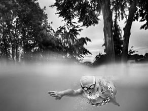B&W image of a young swimmer underwater blowing bubbles through her nose