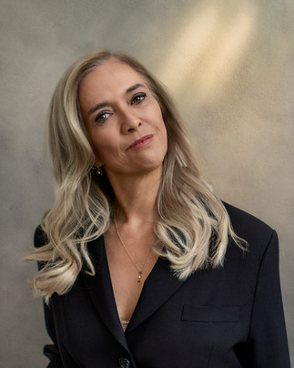 Blonde business woman with her head tilted to one side in a business portrait wearing a black suit jacket