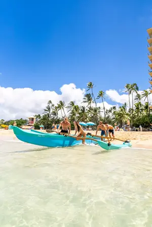 Friends smiling on the shore with an outrigger canoe at Waikīkī Beach