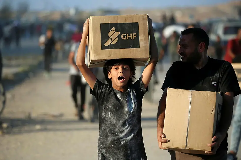People carrying aid parcels, walk along the Salah al-Din road near the Nusseirat refugee camp in the northern Gaza Strip, used by food-seeking Palestinians to reach an aid distributution point set up by the privately-run Gaza Humanitarian Foundation (GHF), on June 25, 2025. (Photo by Eyad BABA / AFP) Credit: AFP/EYAD BABA
