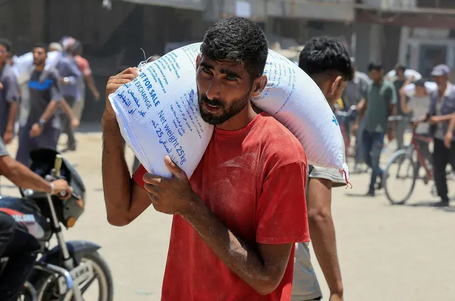 A Palestinian carries a sack of flour as people gather to receive aid supplies in Khan Younis, in the southern Gaza Strip, June 26, 2025. REUTERS/Hatem Khaled Credit: Hatem Khaled/רויטרס