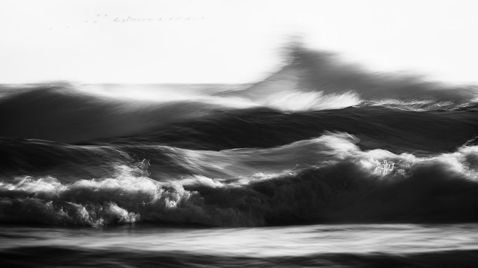Black-and-white blurred ocean waves crashing in a wild seascape, with foamy surf and a dramatic, turbulent mood