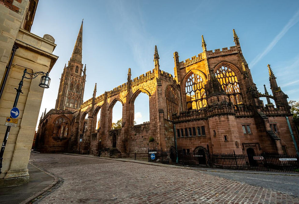 View of Coventry Cathedral ruins with its spire and sunlit Gothic architecture against a clear blue sky