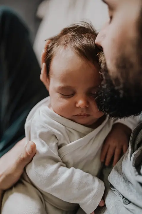 Neugeborenes schläft sicher in den Armen seines Papas während eines Newbornshootings in 1230 Wien, fotografiert von Pia Morpurgo Fotografie.