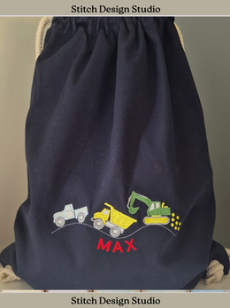 A navy blue bag with a truck, a dumper truck and a digger embroidered in different colours on the front. Underneath is the name Max in red thread.