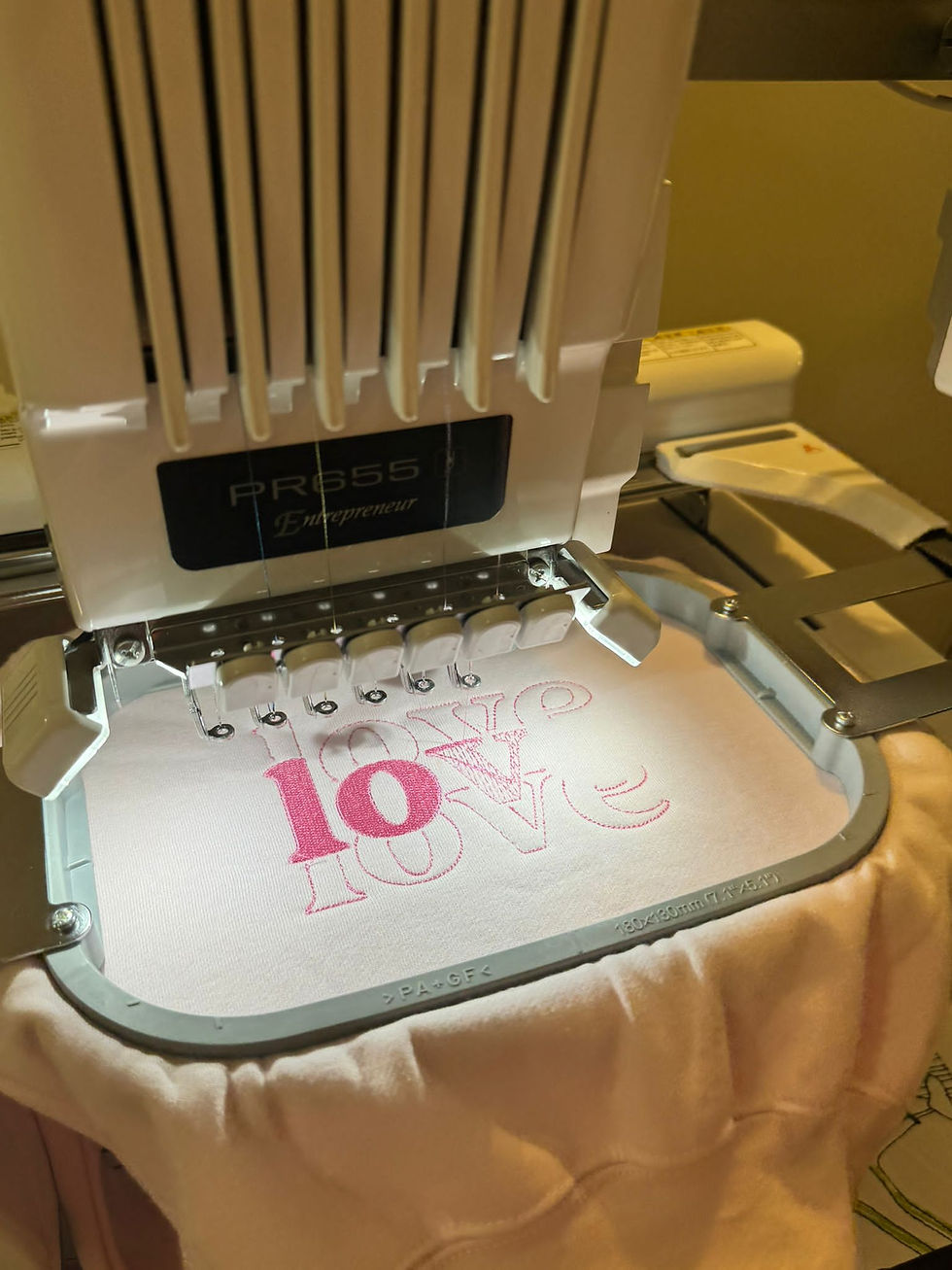 Thumbnail: An embroidery machine with the hoop in and a pink children's sweatshirt being embroidered with the word 'LOVE' in capitals.