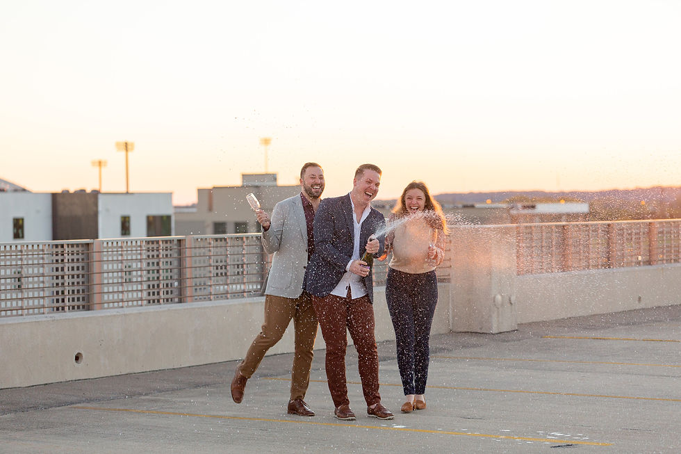 The BKP Team—Hannah Thomsen, Brandon Kane, and Forest Kane—popping a bottle of champagne on a rooftop in Davenport, Iowa. Captured by Brandon Kane Photography, expert Iowa City wedding photographers known for celebrating and capturing joyful moments.