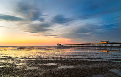 Southport Pier at low tide during sunset with golden reflections on wet sand and dramatic clouds overhead