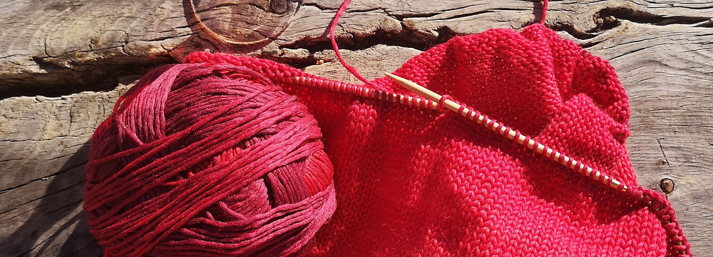 ein Glas Rotwein und ein Strickprojekt mit roter Wolle