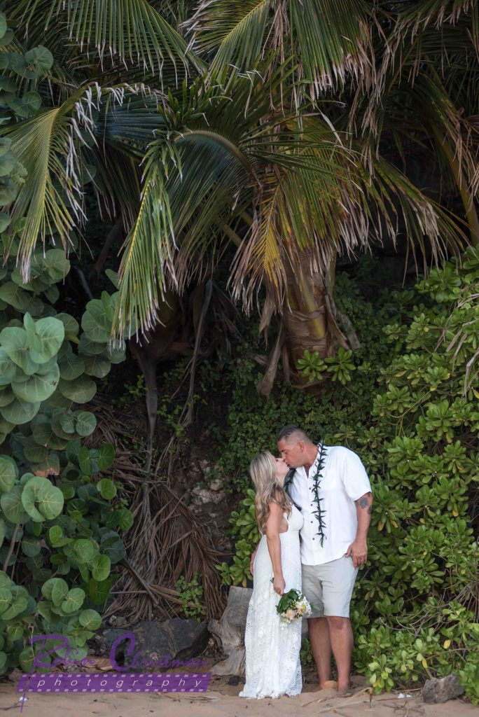 Couple kiss under tall palm tree on maui beach after vow renewal ceremony