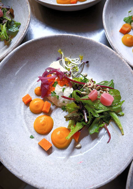 Auf einem Teller sind Salat und Weichkäse aufwendig angerichtet.