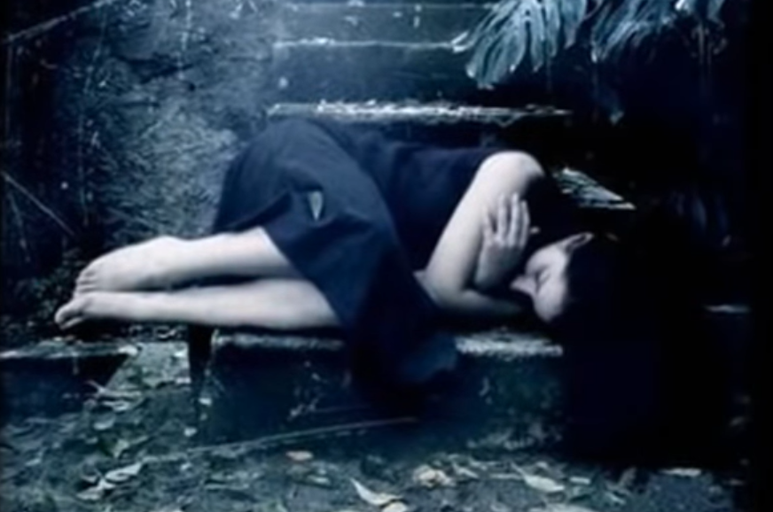 Femme en robe bleue couchée en fœtus sur un banc