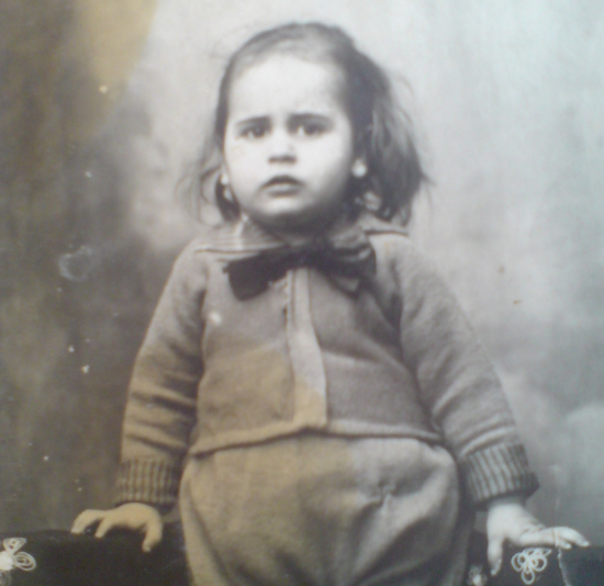 Photo de Léon enfant, un nœud orne son col, cheveux longs et mains posées de chaque côté