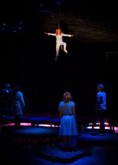 Performer in a blue suit with dog ears suspended above the stage while other performers look on from the ground (Flying V Theatre)