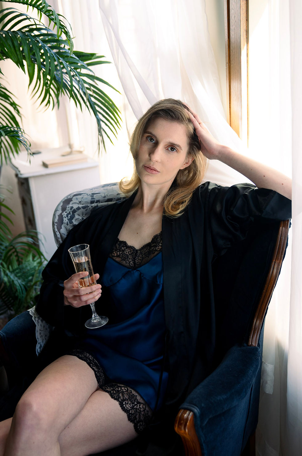Thumbnail: Model seated in a navy silk and lace slip with black robe, holding a glass in a relaxed setting.