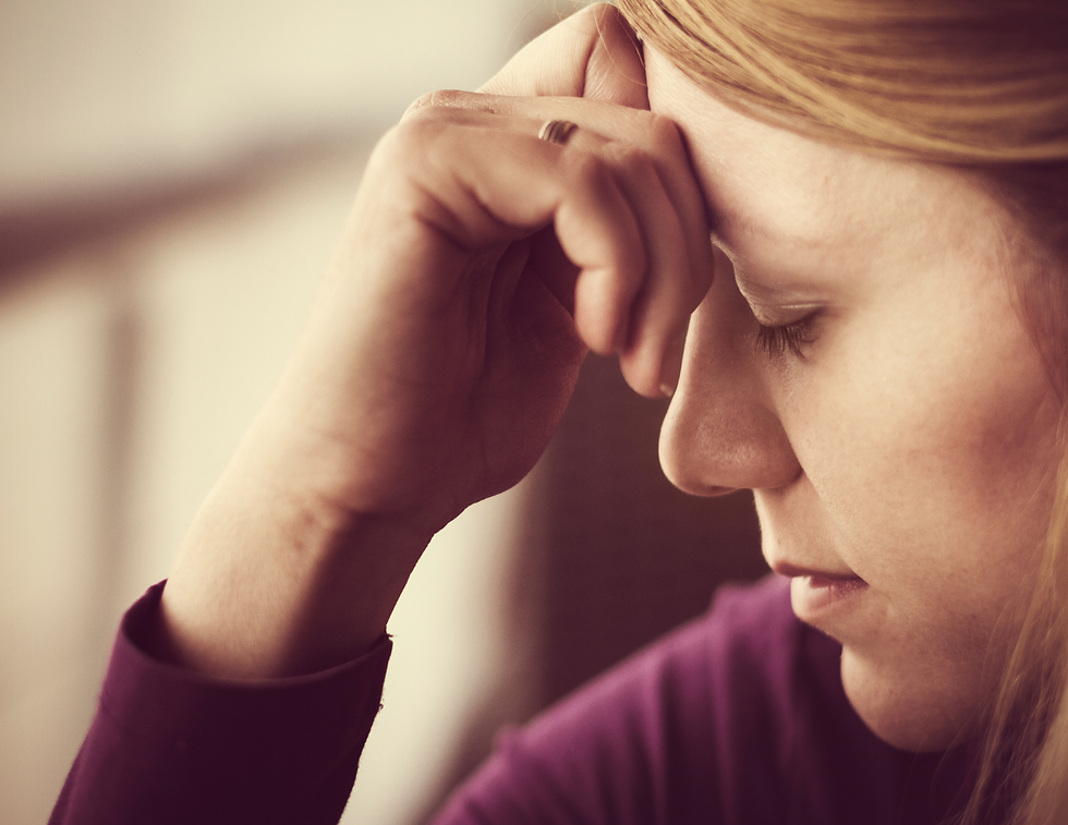 A woman in a purple sweater holds her forehead, eyes closed, appearing stressed. The background is softly blurred and neutral in color.