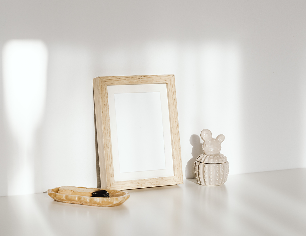 Wooden photo frame beside a ceramic cactus-shaped jar on a white shelf; soft sunlight casts shadows, creating a calm atmosphere.