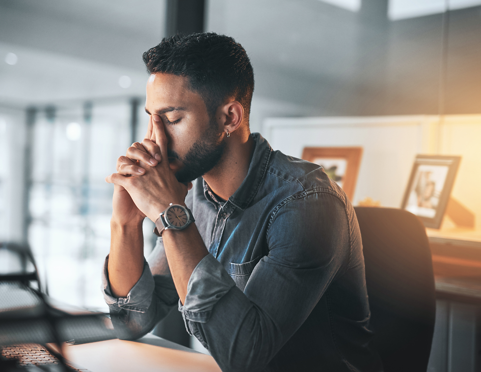 Man in denim shirt sits at a desk in an office, deep in thought. Soft lighting, framed photos and a modern setting create a contemplative mood.
