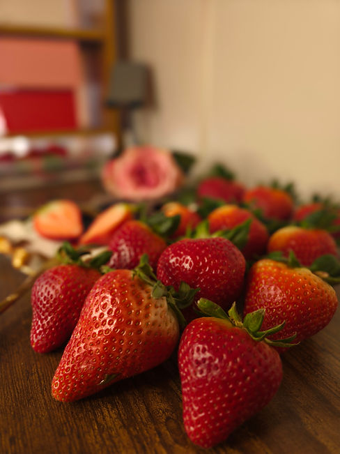 A close-up, high-angle shot of premium raw ingredients for Wilkes-Berry artisan gifts, featuring vibrant red strawberries and a soft pink rose in the background