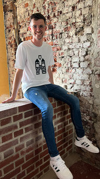 Miniaturbild: Ein junger Mann sitzt auf einer Backsteinmauer und trägt ein Trigema T-Shirt in weiß. Auf der Brust ist der Hachenburger Turm in grün aufgedruckt.