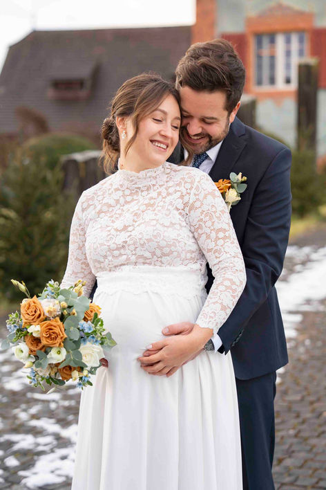 Bräutigam umarmt die schwangere Braut bei einer Winterhochzeit in Luzern