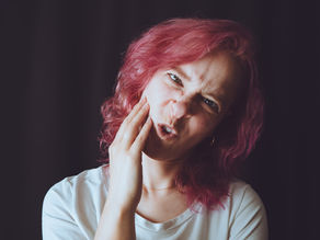 Vrouw met roze haar voor een zwarte achtergrond die een gek gezicht trekt en in de camera kijkt