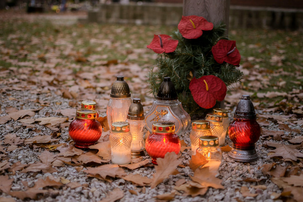 Candles on gravel, surrounded by fallen leaves and red flowers, glow warmly at dusk, creating a peaceful, memorial atmosphere. Seasonal Tributes.