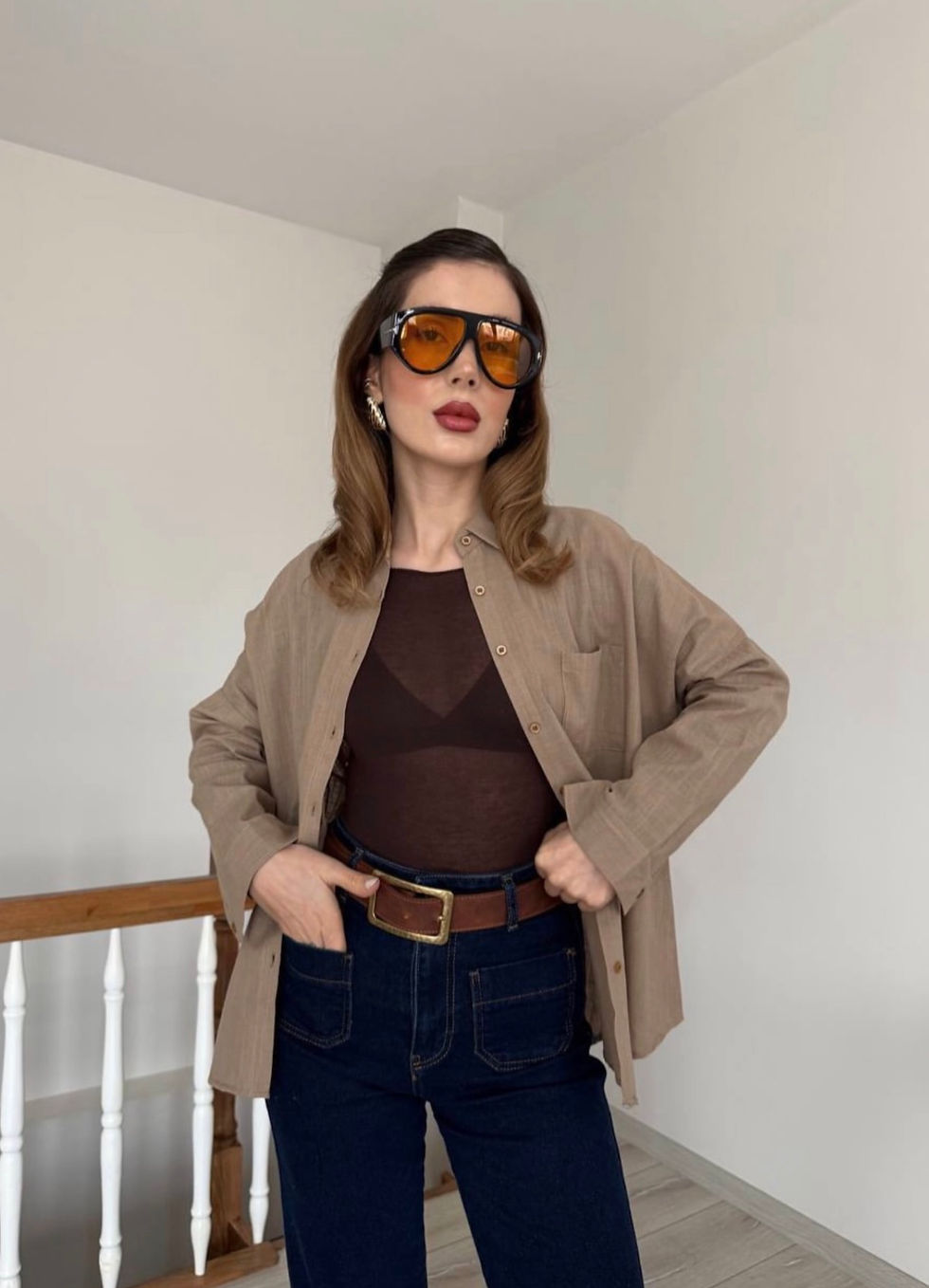 Thumbnail: Woman in brown open shirt, sheer top, jeans, and orange sunglasses.