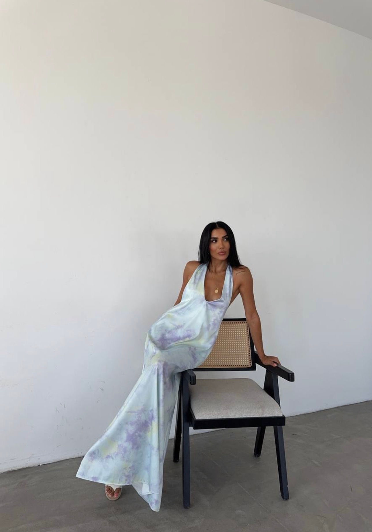 Woman in tie-dye halter dress, leaning on chair.