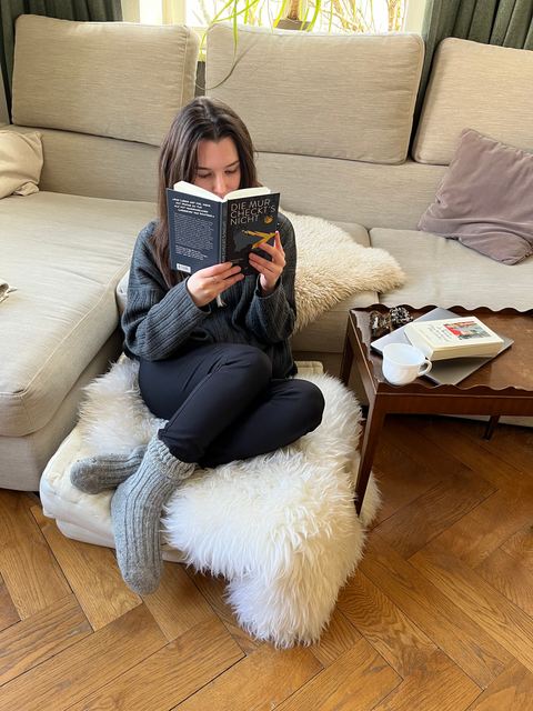 A woman sitting on a pillow reading "Die Mur checkt's nicht" by Christoph Fromm
