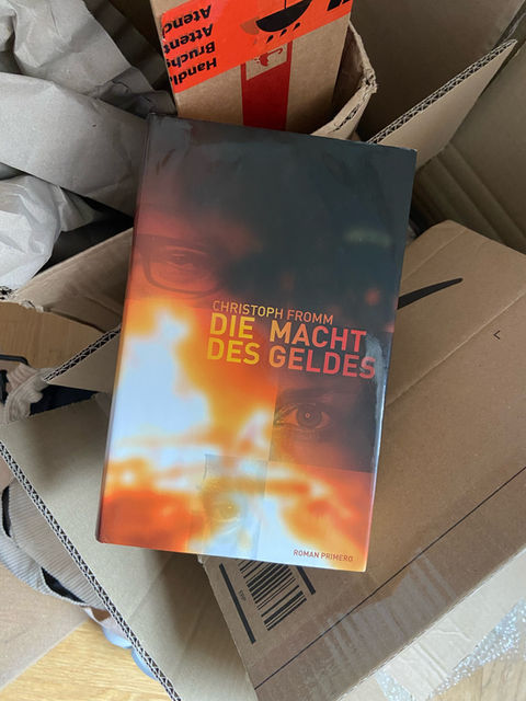 The book "Die Macht des Geldes" by Christoph Fromm lying on a pile of cardboard boxes