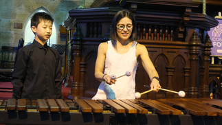 A woman tries the marimba as a young percussionist looked on