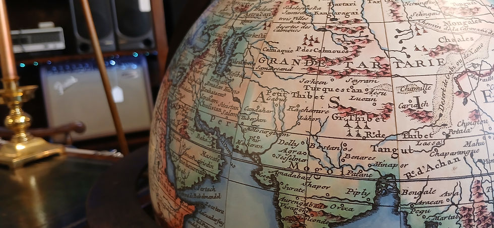 Close-up of an antique globe with old map labels like Grand Tartarie and Tibet, in a dim study beside a brass lamp.