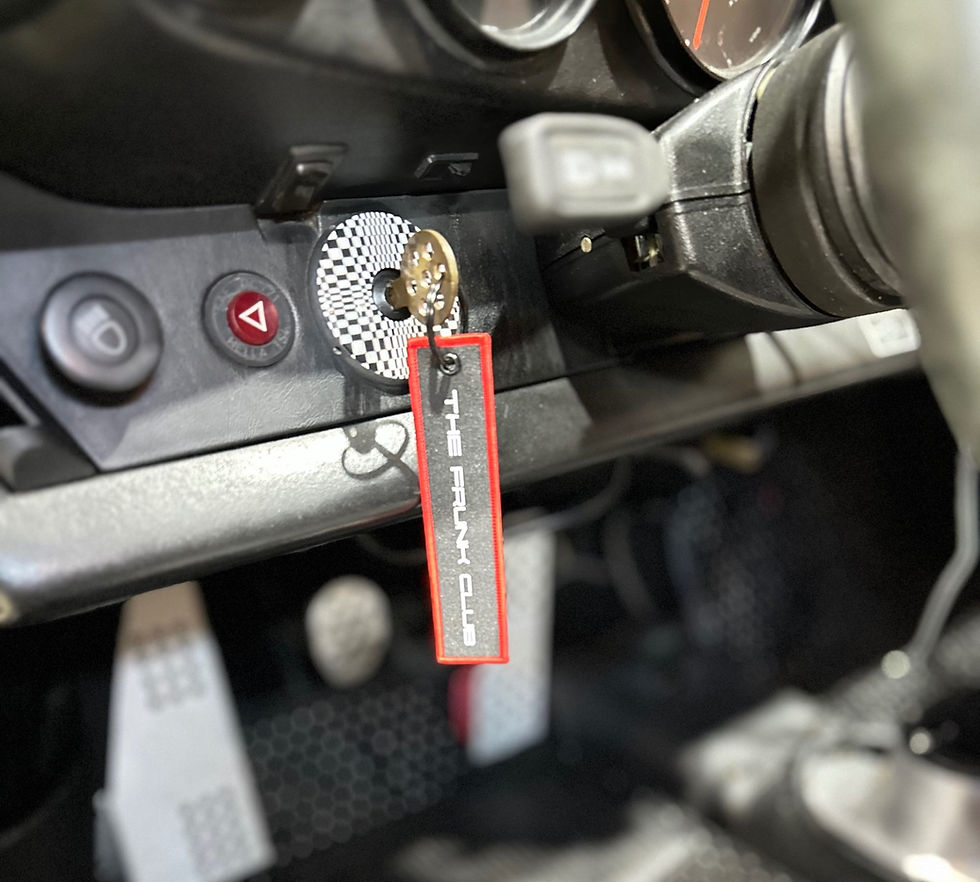 Fabric key tag attached to a car key in the ignition, featuring red borders and “THE FRUNK CLUB” embroidered in silver.