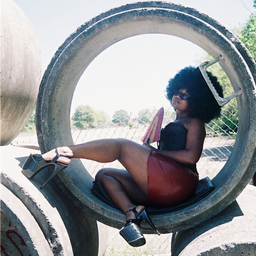 black woman sitting in a concrete circle with fan and large heels