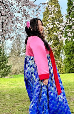 Tifa in Hanbok dress is standing in front of a cherry blossom tree .