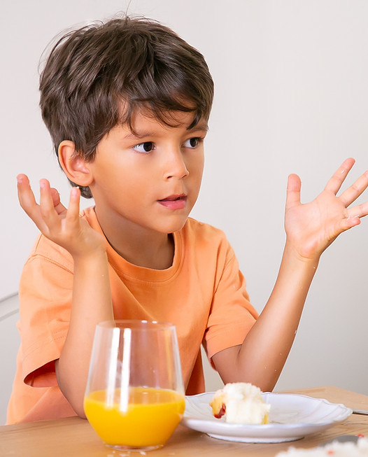 Smiling young boy sitting and eating birthday cake while drinking orange juice.
