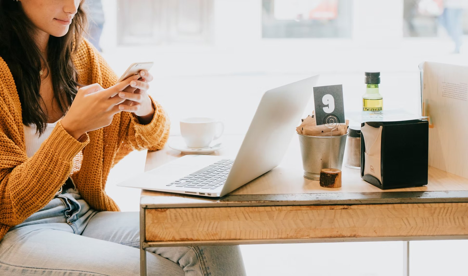Woman using her phone at a café table with a laptop