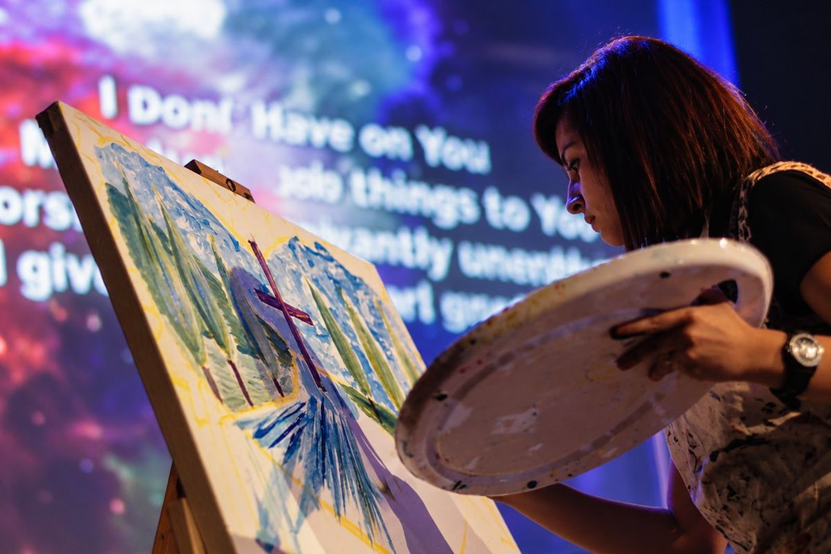 Alexa painting a cross and trees live on stage during a worship service