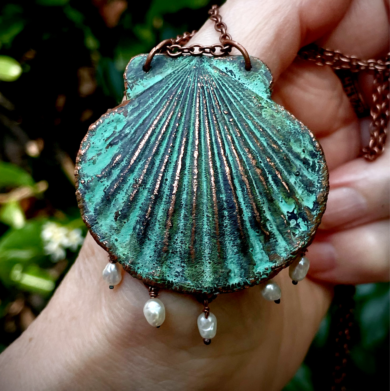 A hand holding green sea shell with pearls pendant