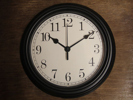 Eine Zeigeruhr mit weissem Ziffernblatt und schwarzen Zahlen auf einem holzigen Hintergrund